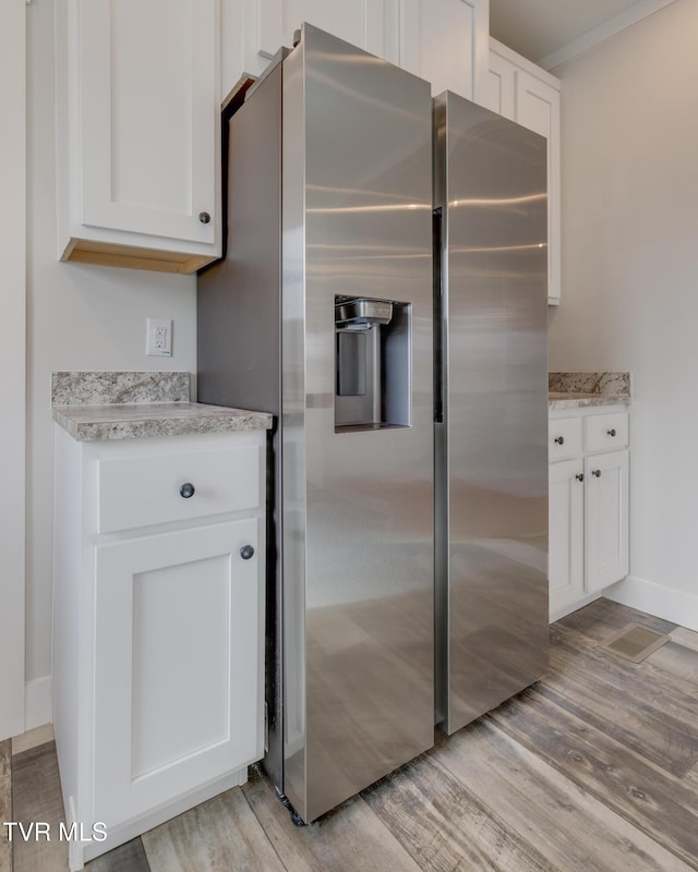 kitchen featuring stainless steel refrigerator with ice dispenser, white cabinetry, crown molding, and light hardwood / wood-style flooring