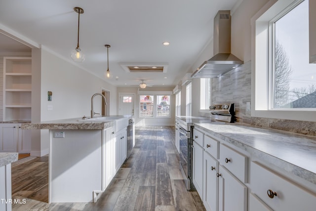 kitchen featuring sink, white cabinetry, hanging light fixtures, appliances with stainless steel finishes, and wall chimney range hood