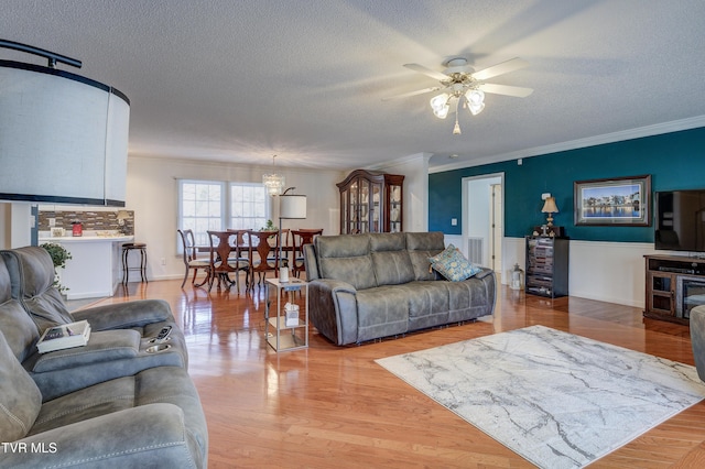 living room featuring ceiling fan, crown molding, light hardwood / wood-style floors, and a textured ceiling