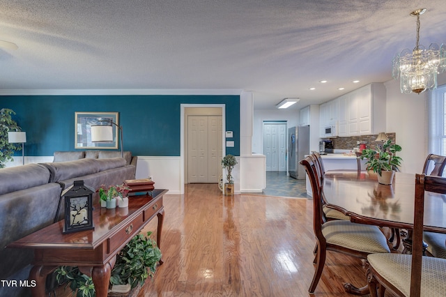 dining area with an inviting chandelier, crown molding, a textured ceiling, and light wood-type flooring