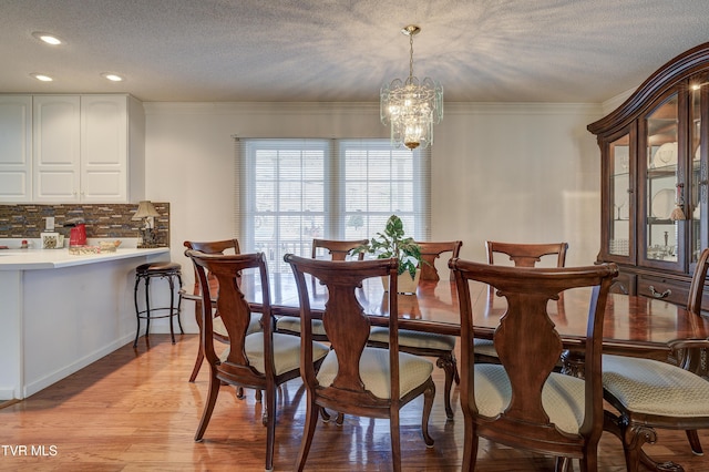 dining space featuring an inviting chandelier, crown molding, light hardwood / wood-style floors, and a textured ceiling