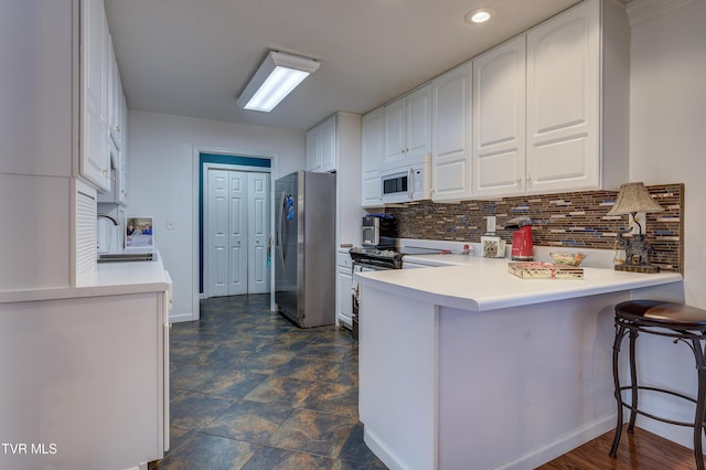 kitchen featuring a breakfast bar, sink, white cabinetry, appliances with stainless steel finishes, and kitchen peninsula