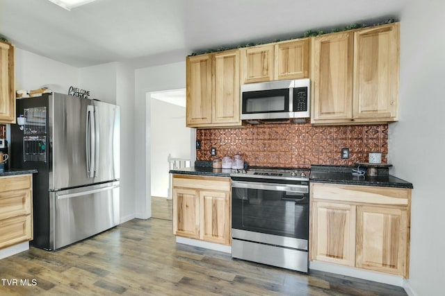 kitchen with appliances with stainless steel finishes, tasteful backsplash, dark stone counters, dark wood-type flooring, and light brown cabinets