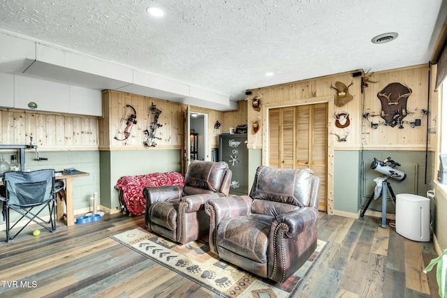 living room with dark wood-type flooring, a textured ceiling, and wood walls