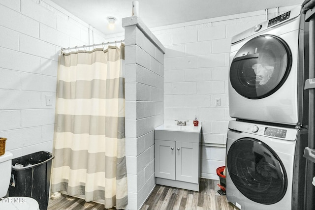 clothes washing area with wood-type flooring, stacked washer and clothes dryer, and sink