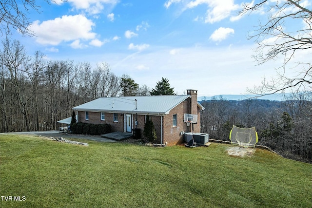 rear view of house featuring a trampoline, central AC unit, and a yard