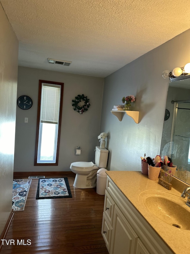 bathroom featuring vanity, wood-type flooring, a textured ceiling, toilet, and walk in shower