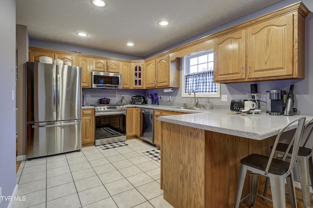 kitchen featuring sink, a breakfast bar area, stainless steel appliances, light tile patterned flooring, and kitchen peninsula