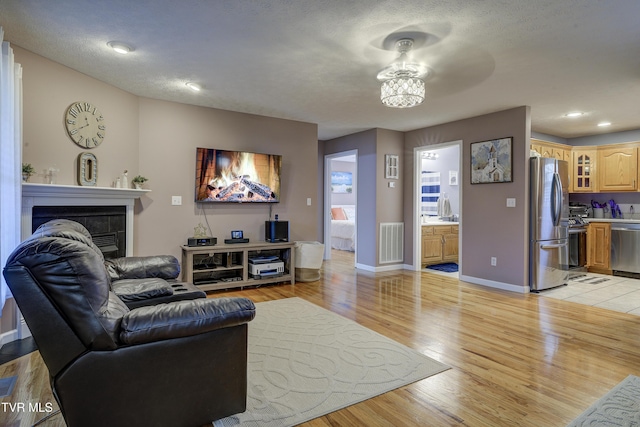 living room featuring a tiled fireplace, a textured ceiling, and light wood-type flooring