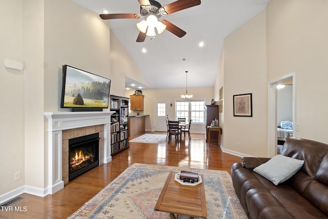 living area featuring visible vents, a tiled fireplace, light wood-style floors, high vaulted ceiling, and baseboards