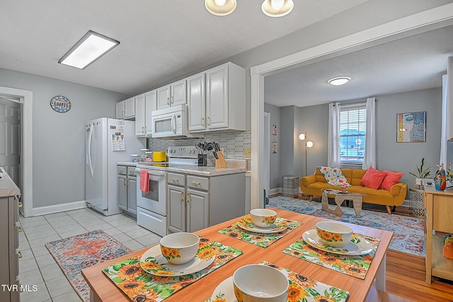 kitchen with light tile patterned flooring, a textured ceiling, white appliances, and decorative backsplash