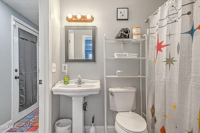 bathroom with sink, curtained shower, toilet, and a textured ceiling