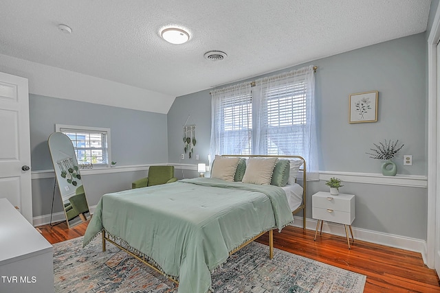 bedroom featuring vaulted ceiling, hardwood / wood-style floors, and a textured ceiling