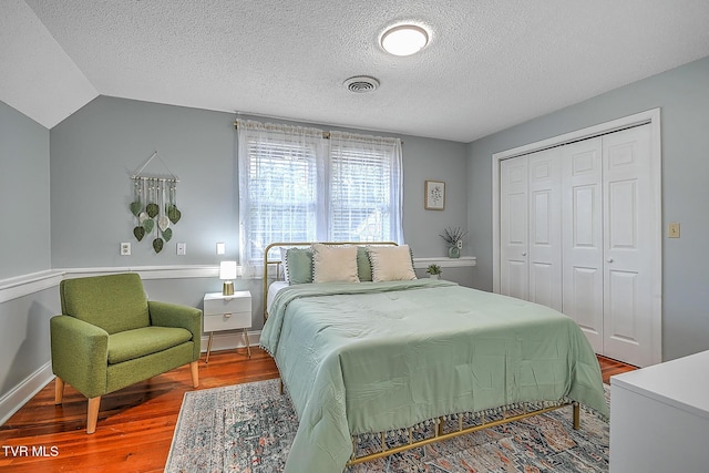 bedroom featuring lofted ceiling, hardwood / wood-style floors, a closet, and a textured ceiling