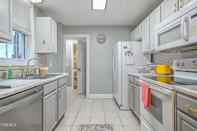 kitchen with sink, white appliances, gray cabinets, light tile patterned floors, and white cabinets