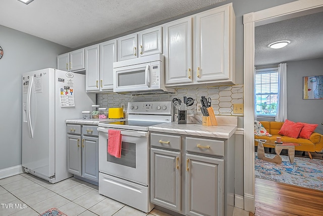 kitchen with gray cabinetry, white appliances, a textured ceiling, and light tile patterned floors