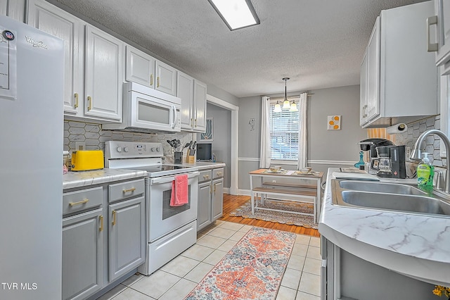 kitchen featuring sink, white appliances, light tile patterned floors, backsplash, and decorative light fixtures