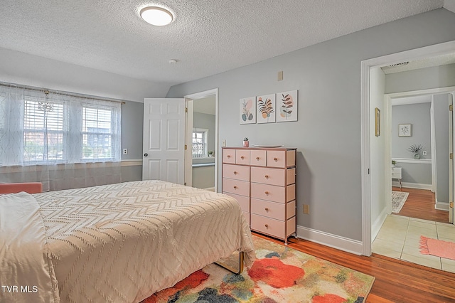 bedroom with wood-type flooring, vaulted ceiling, and a textured ceiling