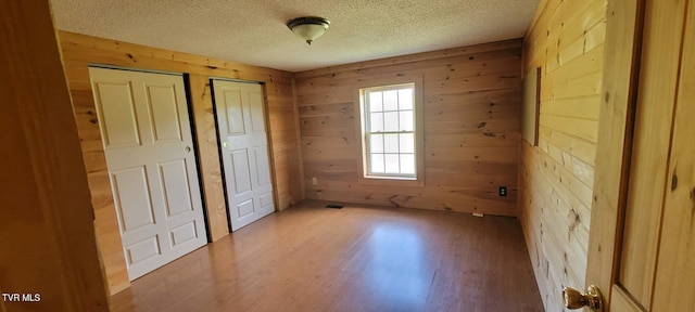 unfurnished bedroom featuring wood-type flooring, a textured ceiling, and wood walls