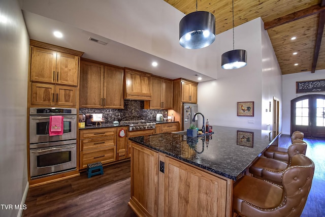 kitchen featuring decorative light fixtures, high vaulted ceiling, an island with sink, stainless steel appliances, and decorative backsplash