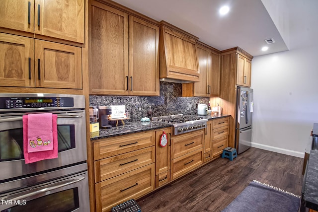 kitchen featuring premium range hood, decorative backsplash, dark stone counters, stainless steel appliances, and dark wood-type flooring