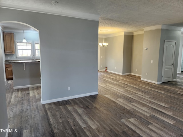 empty room with crown molding, a chandelier, a textured ceiling, and dark hardwood / wood-style flooring