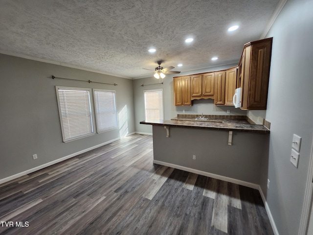 kitchen featuring ornamental molding, kitchen peninsula, a textured ceiling, and a kitchen bar