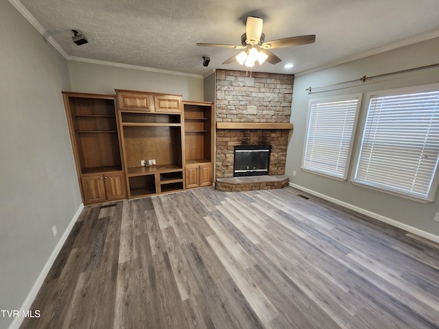 unfurnished living room featuring a textured ceiling, ornamental molding, hardwood / wood-style flooring, ceiling fan, and a fireplace