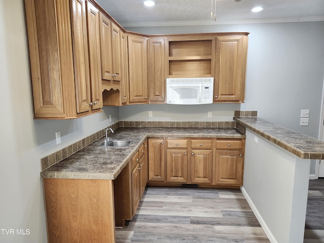 kitchen with sink, ornamental molding, kitchen peninsula, and light wood-type flooring