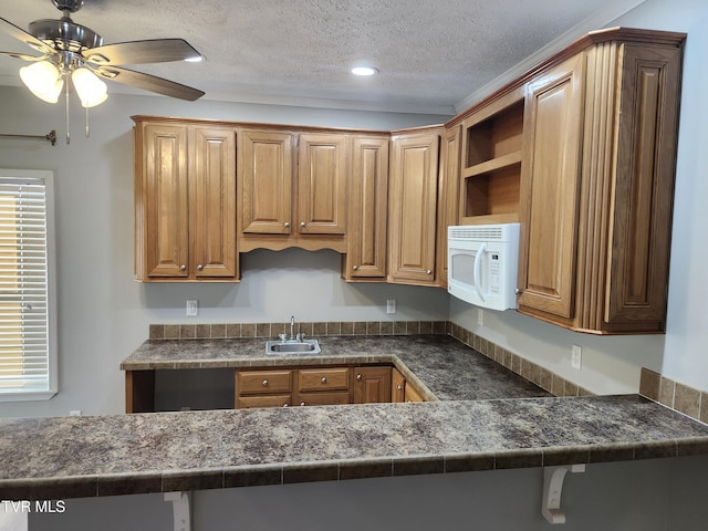 kitchen featuring ceiling fan, kitchen peninsula, sink, and a textured ceiling