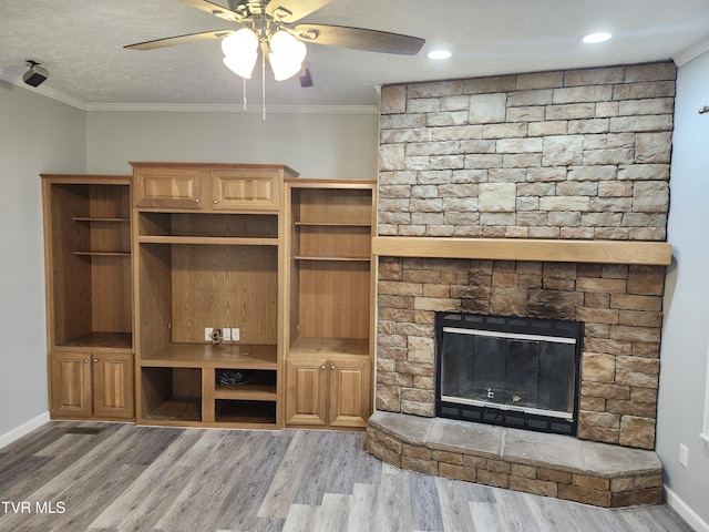 unfurnished living room featuring crown molding, ceiling fan, a stone fireplace, and hardwood / wood-style flooring