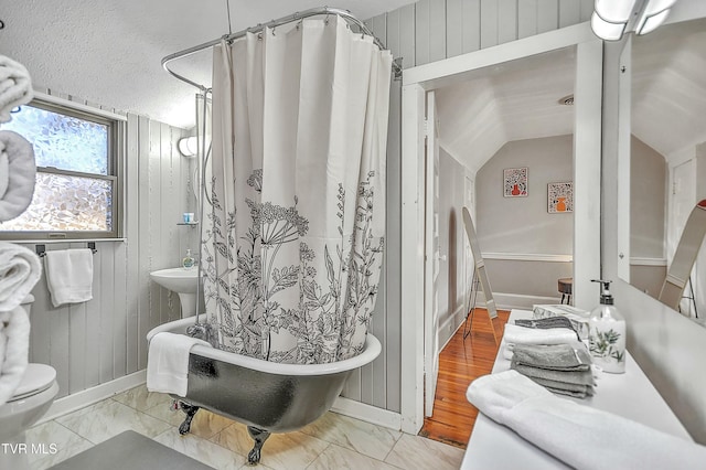 bathroom featuring vaulted ceiling, wooden walls, toilet, a textured ceiling, and shower / bath combo with shower curtain