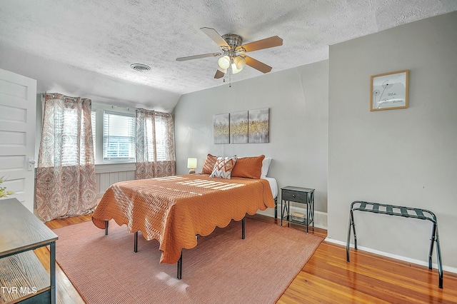 bedroom with hardwood / wood-style floors, vaulted ceiling, a textured ceiling, and ceiling fan