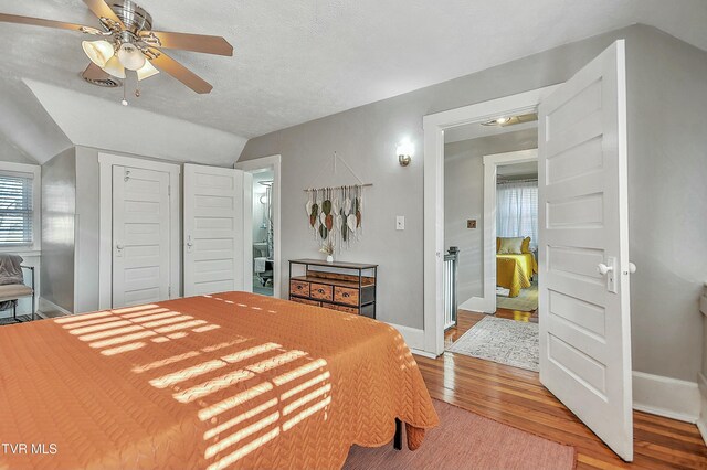 bedroom with lofted ceiling, a textured ceiling, a closet, ceiling fan, and hardwood / wood-style floors