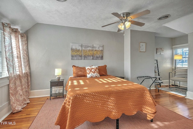 bedroom with ceiling fan, lofted ceiling, light hardwood / wood-style flooring, and a textured ceiling