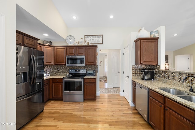 kitchen featuring sink, light wood-type flooring, light stone countertops, and appliances with stainless steel finishes