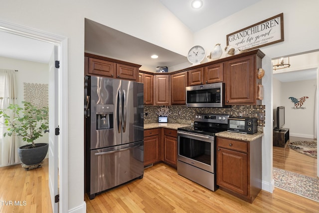 kitchen with light stone counters, appliances with stainless steel finishes, light wood-type flooring, and backsplash