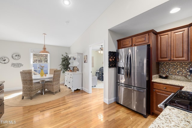 kitchen with lofted ceiling, appliances with stainless steel finishes, light stone countertops, light hardwood / wood-style floors, and decorative backsplash