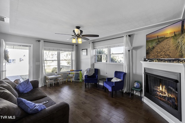 living room with dark wood-type flooring, ceiling fan, and a textured ceiling