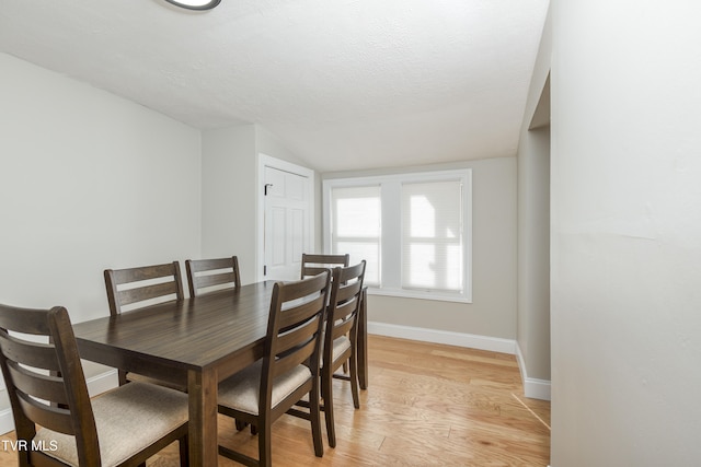 dining space with vaulted ceiling, a textured ceiling, and light hardwood / wood-style floors