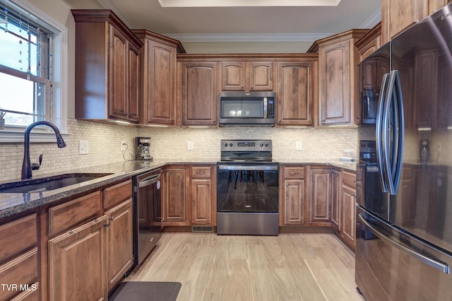 kitchen with sink, backsplash, stainless steel appliances, dark stone counters, and light wood-type flooring