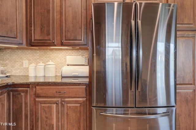 kitchen featuring dark stone countertops, stainless steel fridge, and backsplash