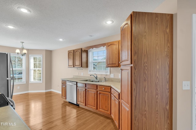 kitchen featuring sink, decorative light fixtures, a textured ceiling, light wood-type flooring, and stainless steel appliances