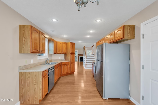 kitchen with appliances with stainless steel finishes, sink, a textured ceiling, and light wood-type flooring