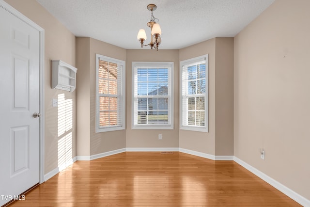 unfurnished dining area featuring an inviting chandelier, light hardwood / wood-style floors, and a textured ceiling