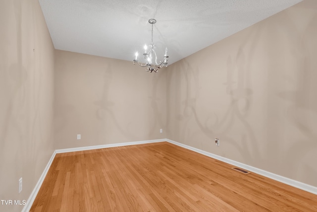 empty room featuring hardwood / wood-style flooring, a chandelier, and a textured ceiling