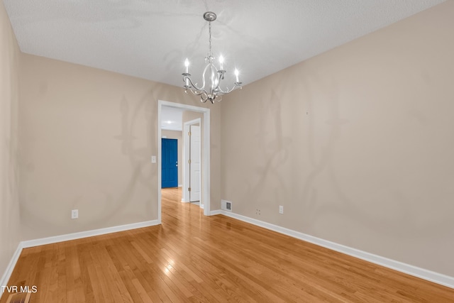 spare room featuring a chandelier, hardwood / wood-style floors, and a textured ceiling