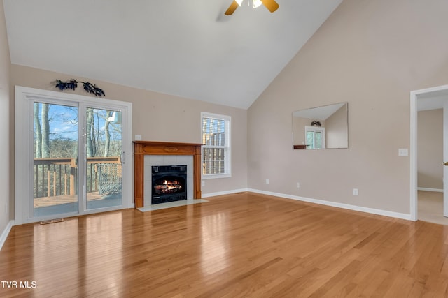 unfurnished living room with ceiling fan, a tiled fireplace, high vaulted ceiling, and light hardwood / wood-style flooring