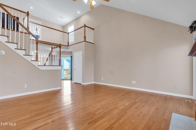 unfurnished living room with a towering ceiling, ceiling fan, and light wood-type flooring