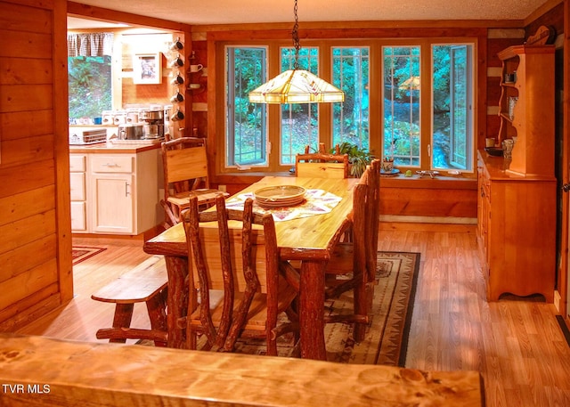 dining space with light wood-type flooring, a textured ceiling, and wood walls